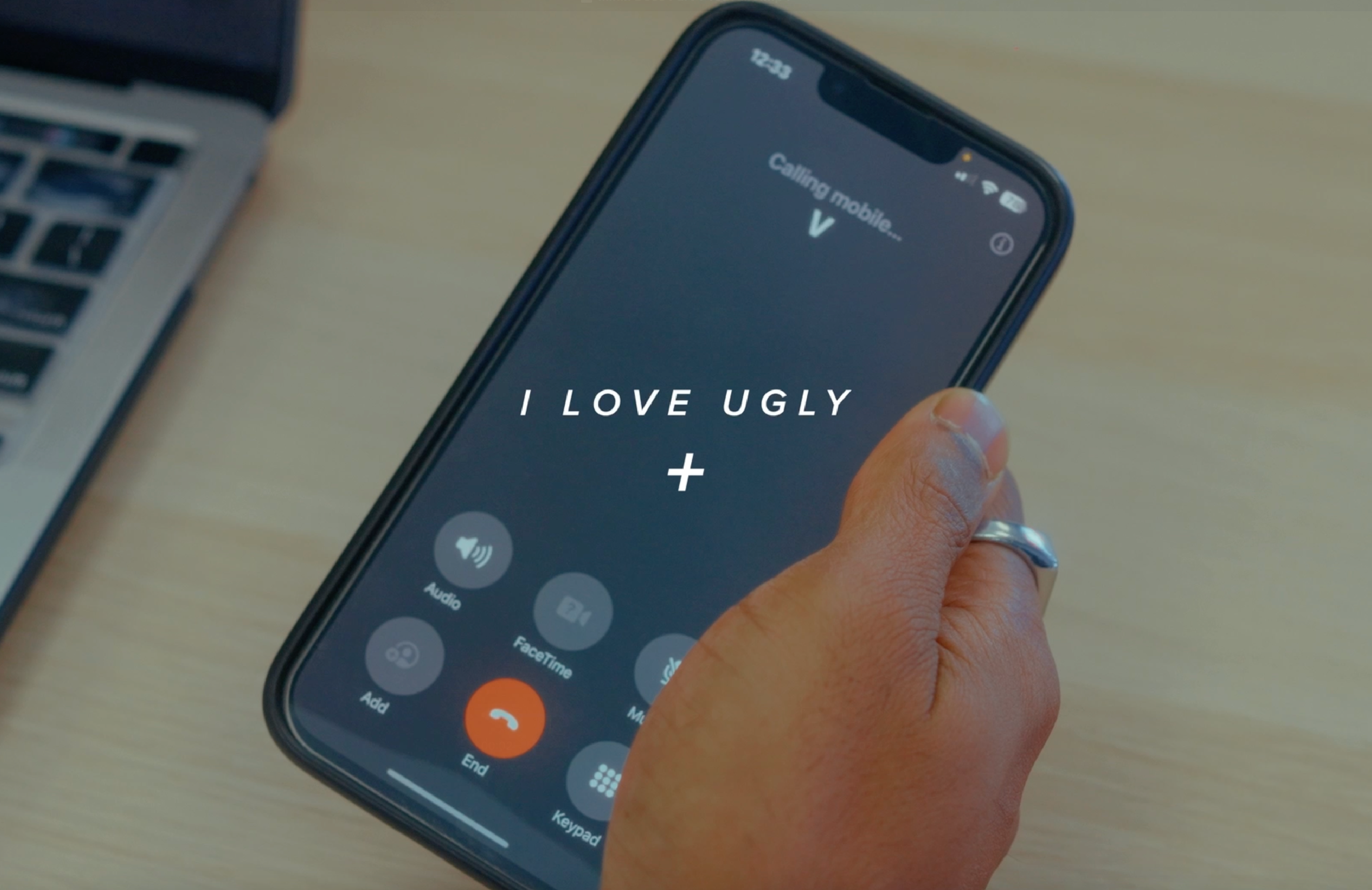 A hand holding a smartphone displaying "I LOVE UGLY" on the screen.